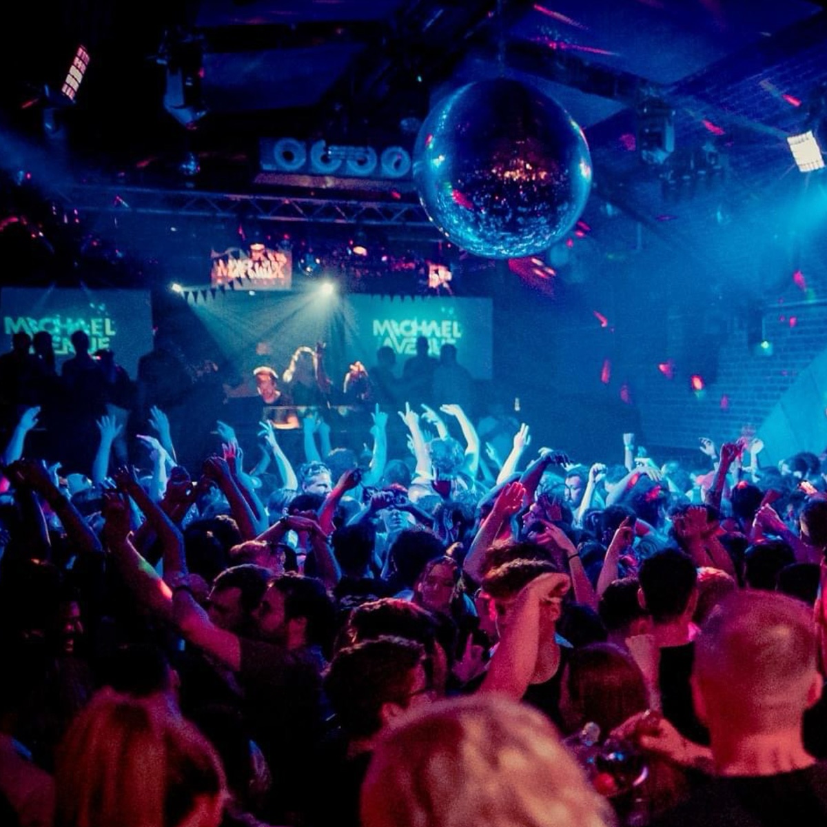 Michael Avenue performing live as a DJ in a vibrant club setting with an energetic crowd.